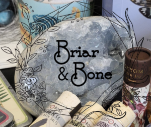 The Briar & Bone logo, which features the words "Briar & Bone" with illustrated leaves and flowers around it, is overlayed on an image of a decorative rock. Other objects beside the rock are out of frame. 